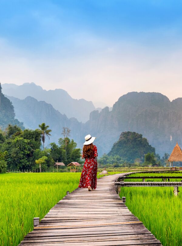 young-woman-walking-wooden-path-with-green-rice-field-vang-vieng-laos (1)